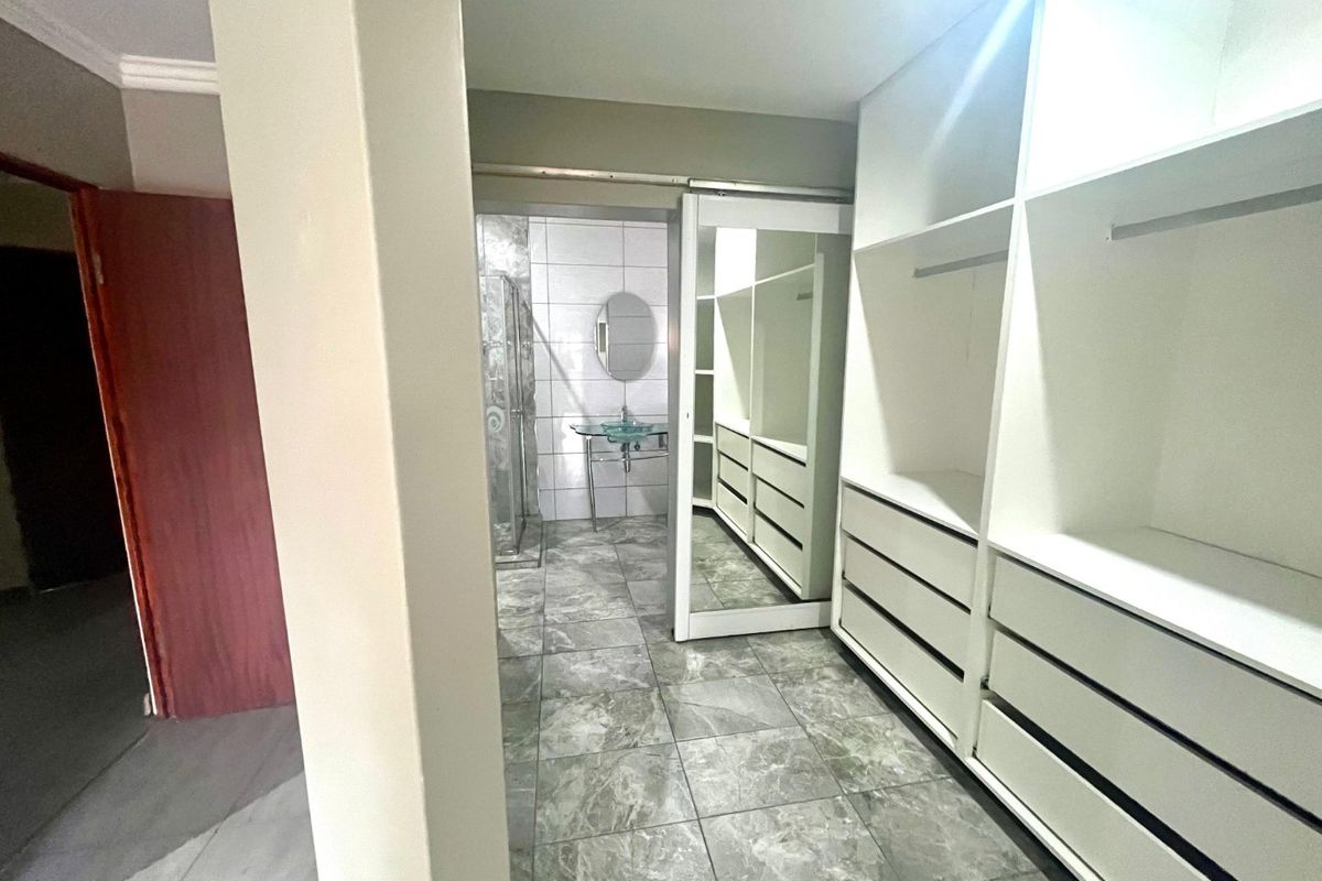 Dressing area featuring extensive built-in cabinetry with sliding mirror doors, leading into an en-suite bathroom with a glass vessel sink and shower.