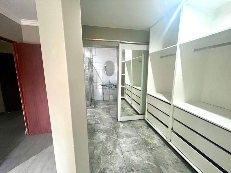 Dressing area featuring extensive built-in cabinetry with sliding mirror doors, leading into an en-suite bathroom with a glass vessel sink and shower.