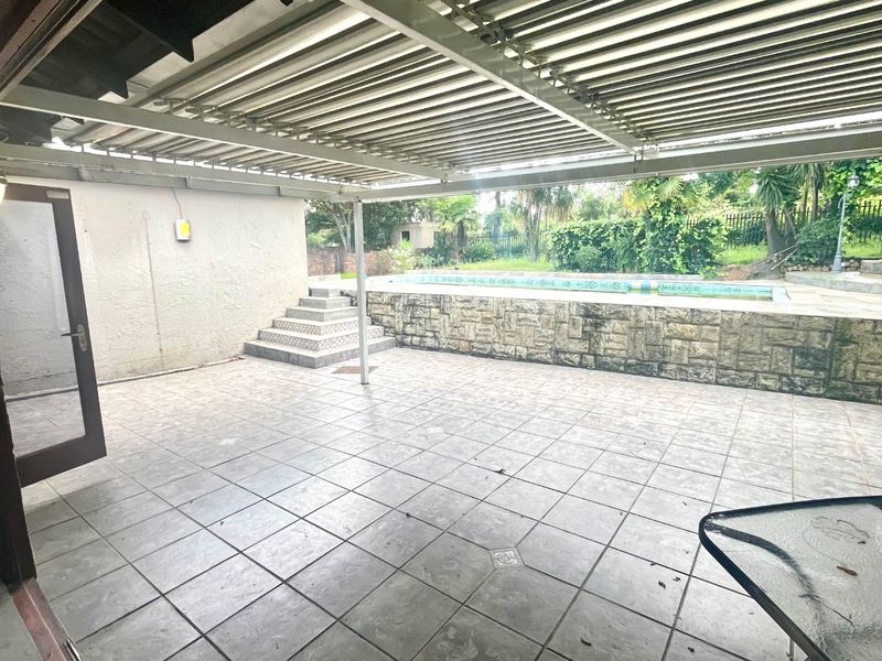 Spacious covered patio area featuring a raised swimming pool with stone cladding and direct access to the garden.