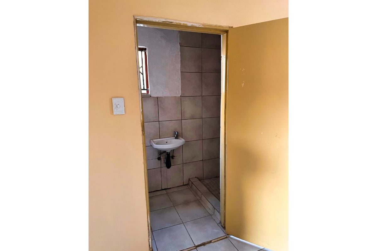 A small, functional bathroom featuring a wall-mounted basin and tiled surfaces, currently in need of cosmetic updates and maintenance.