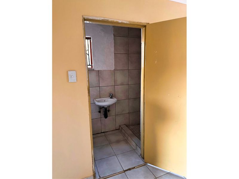 A small, functional bathroom featuring a wall-mounted basin and tiled surfaces, currently in need of cosmetic updates and maintenance.
