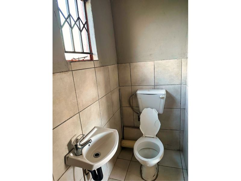 A small, functional bathroom featuring a wall-mounted basin and toilet, with tiled surfaces and a window fitted with a security gate.