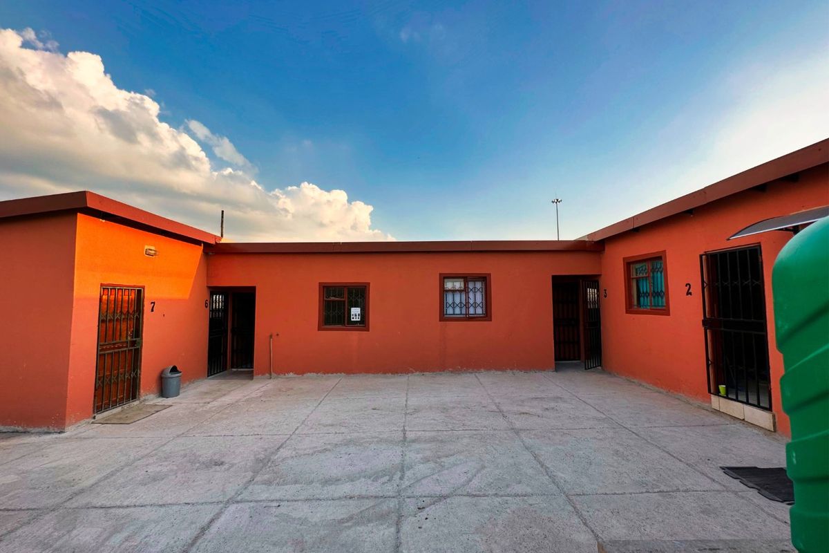 A rear courtyard area featuring concrete paving and multiple access points with security gates and bars, providing functional outdoor space for the property.