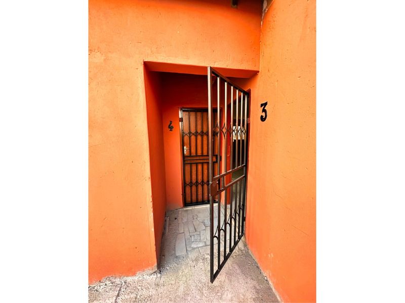 Entrance area featuring a security gate and metal door, showing signs of wear on the exterior walls.