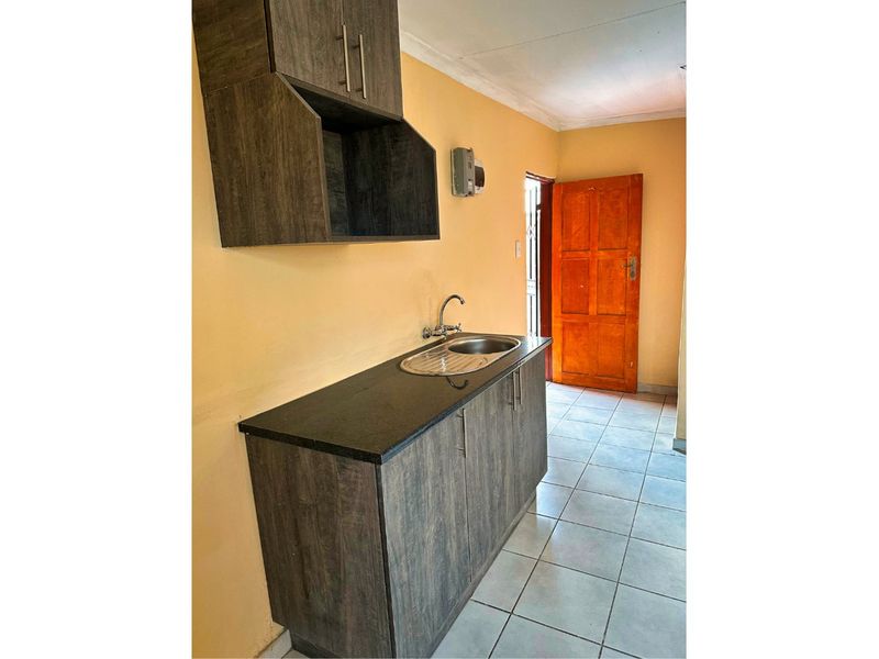 A compact kitchen area featuring dark wood-look cabinetry, a stainless steel sink, and tiled flooring, providing a functional space for food preparation.