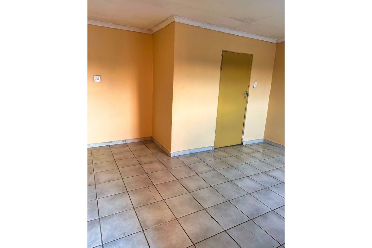 An empty living area featuring neutral ceramic floor tiles, painted walls, and a standard interior door.