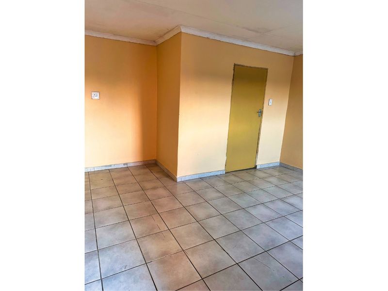 An empty living area featuring neutral ceramic floor tiles, painted walls, and a standard interior door.