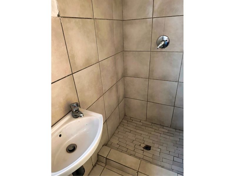 A compact bathroom featuring a wall-mounted basin and a tiled shower area with a single mixer tap.