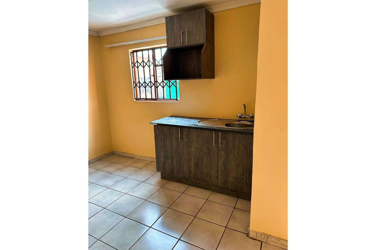 A compact kitchen area featuring dark wood-look cabinetry, a stainless steel sink, and tiled flooring, ready for modernization.