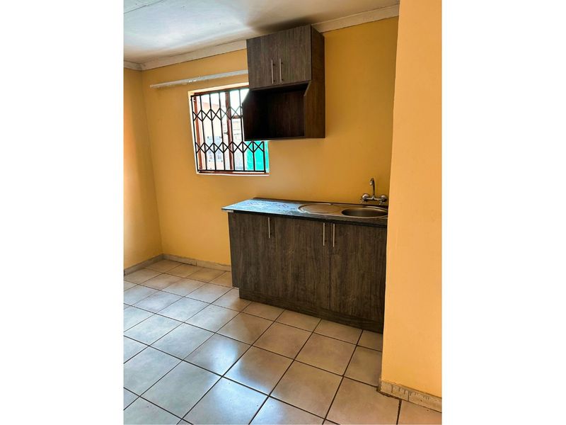 A compact kitchen area featuring dark wood-look cabinetry, a stainless steel sink, and tiled flooring, ready for modernization.