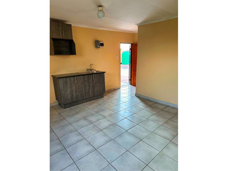 A compact, empty kitchen area featuring basic cabinetry, a sink, and tiled flooring, with direct access to the exterior.