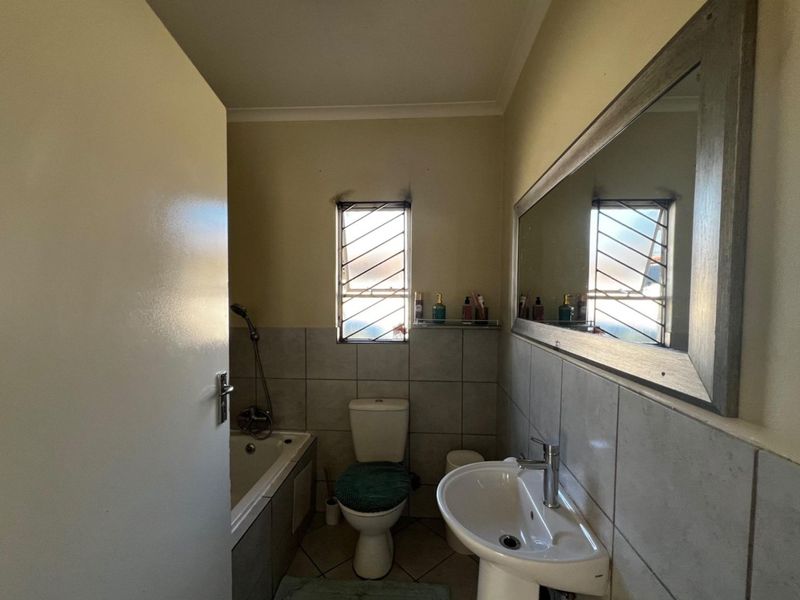 A functional bathroom featuring a pedestal basin, toilet, and bathtub with tiled finishes and security bars on the window.