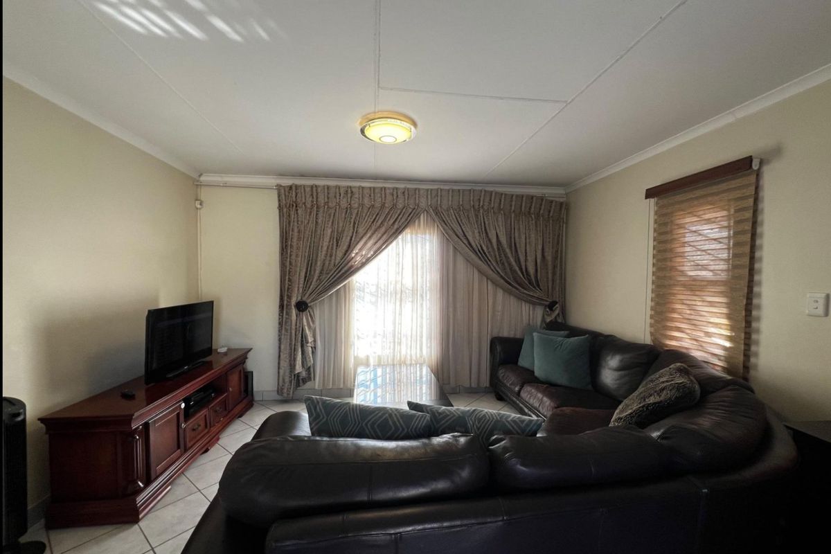 A comfortable living room featuring tiled flooring, neutral wall finishes, and window treatments, providing a functional and well-lit space for relaxation.
