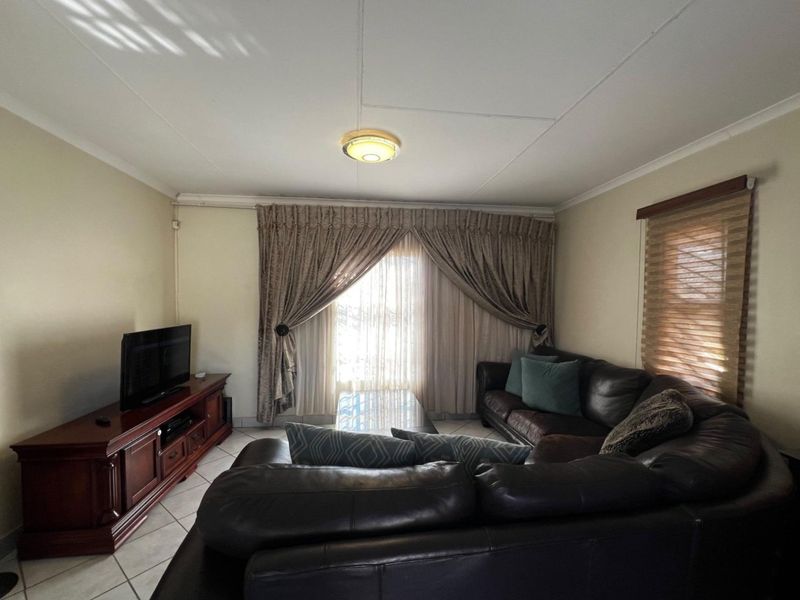 A comfortable living room featuring tiled flooring, neutral wall finishes, and window treatments, providing a functional and well-lit space for relaxation.
