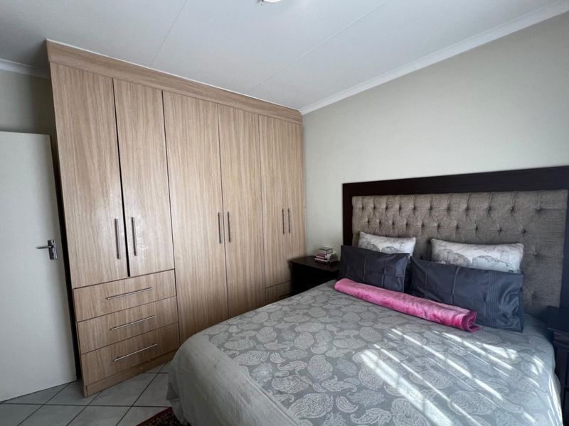 A well-maintained bedroom featuring extensive light wood built-in cupboards and neutral tiled flooring.