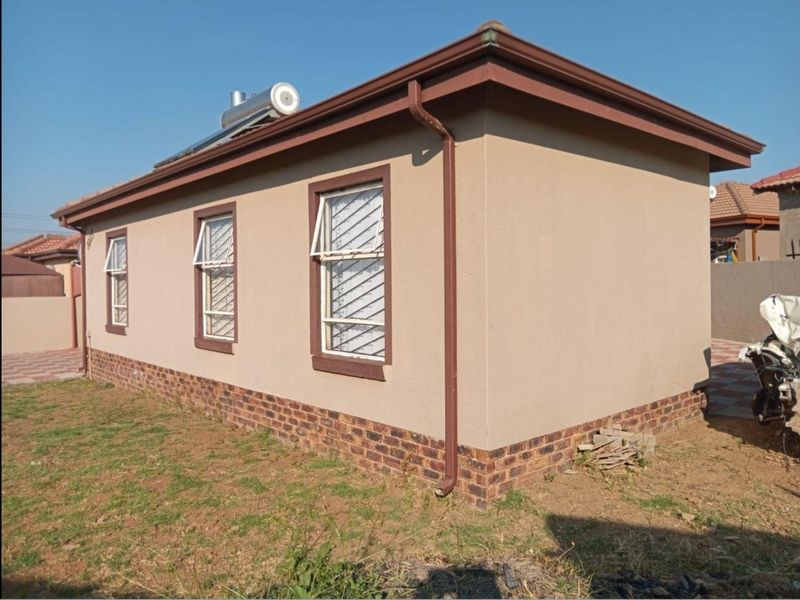 Side view of the house exterior featuring a brick plinth, solar water heater, and security-fitted casement windows.