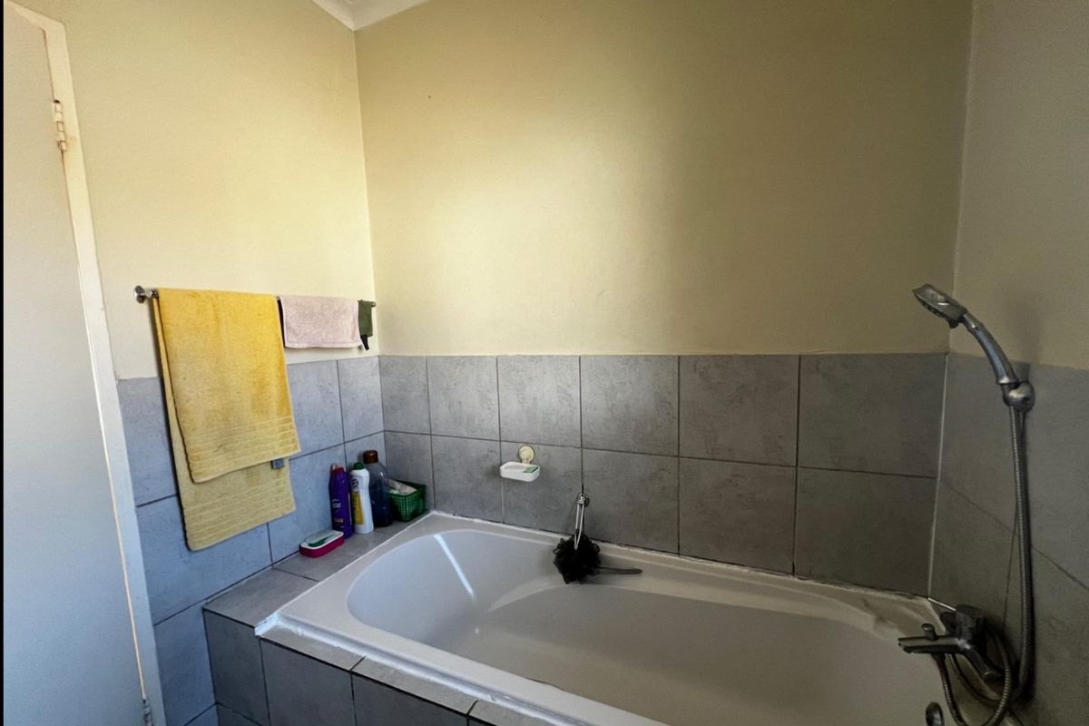 A functional bathroom featuring a built-in bathtub with a shower mixer and tiled splashback, providing a practical space for daily use.