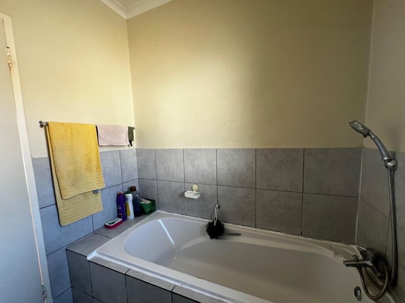 A functional bathroom featuring a built-in bathtub with a shower mixer and tiled splashback, providing a practical space for daily use.