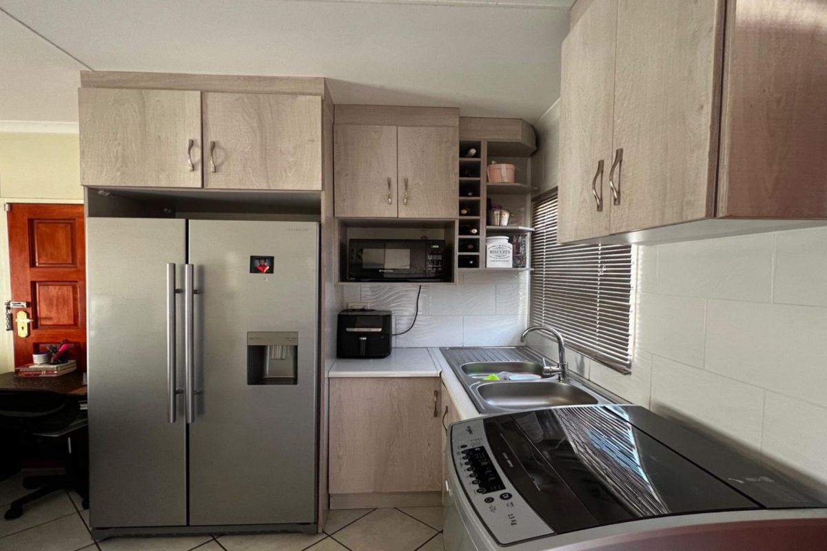 A functional kitchen featuring light wood-look laminate cabinetry, a built-in microwave, a stainless steel double sink, and a tiled backsplash.