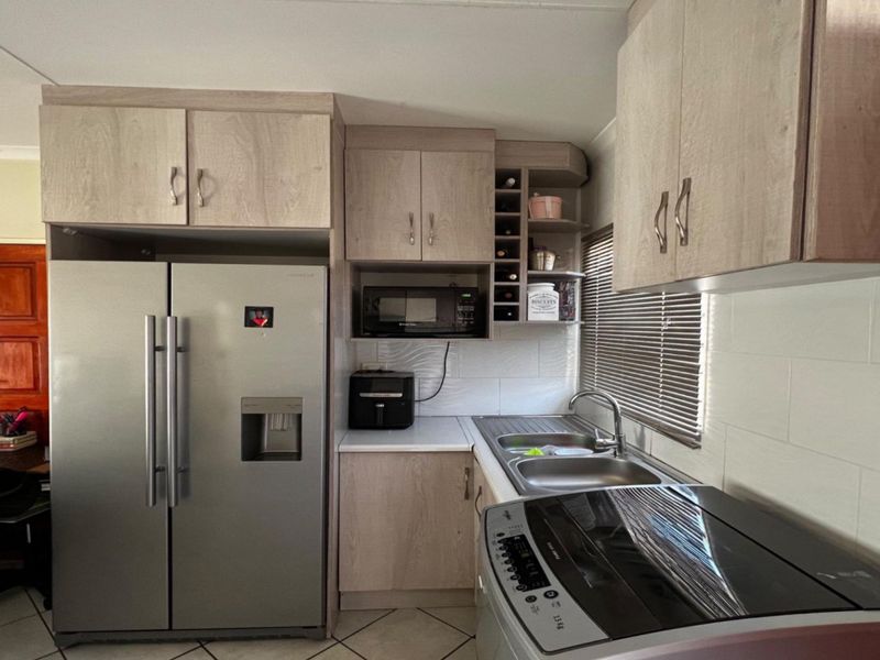 A functional kitchen featuring light wood-look laminate cabinetry, a built-in microwave, a stainless steel double sink, and a tiled backsplash.