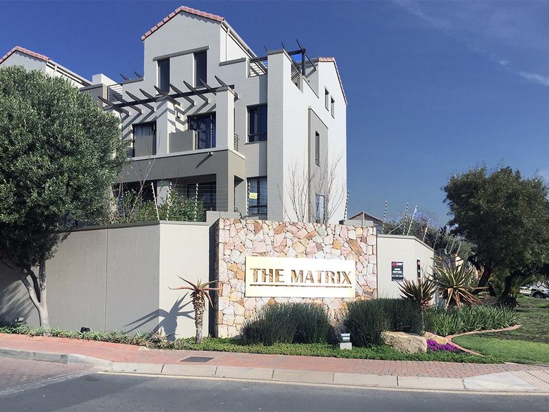 Exterior view of The Matrix apartment complex featuring stone cladding, modern architectural design, balconies with pergolas, and secure perimeter fencing.