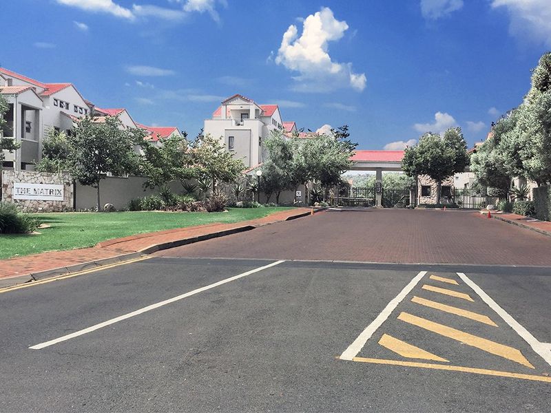 Street view of the entrance to The Matrix apartment complex, featuring a paved driveway, security gate, and well-maintained landscaped grounds.