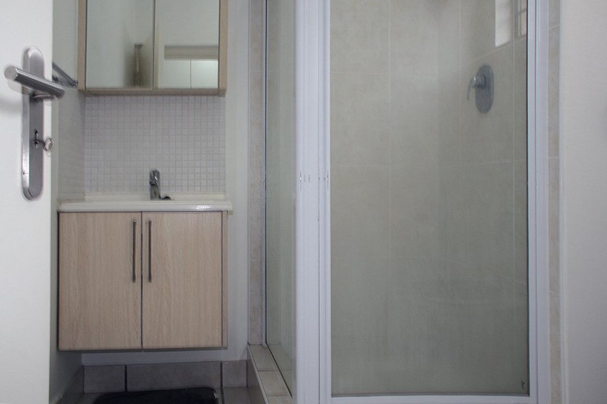 A functional bathroom featuring a vanity cabinet with basin, mirrored storage, and a glass-enclosed shower with tiled finishes.