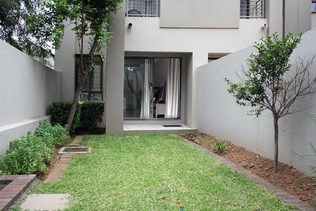 A private rear courtyard featuring a small lawn, paved garden borders, and direct access to the interior via a sliding glass door.