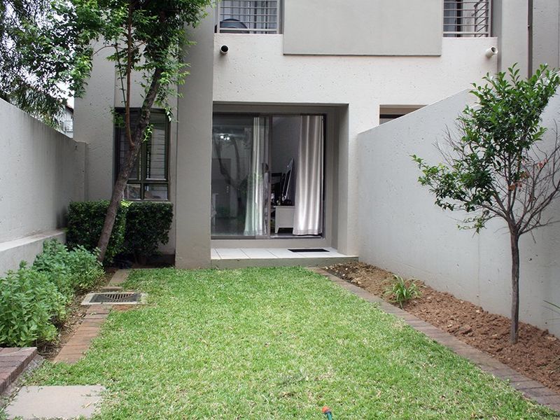 A private rear courtyard featuring a small lawn, paved garden borders, and direct access to the interior via a sliding glass door.