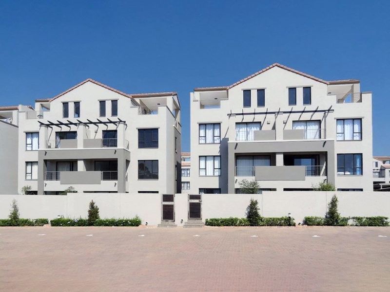 Front elevation view of a modern multi-story apartment complex featuring paved parking, private balconies, and structured architectural detailing.