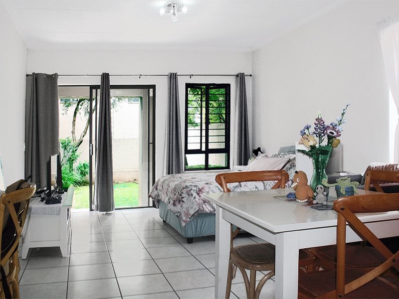 Open-plan living and sleeping area featuring tiled flooring, a sliding glass door providing garden access, and security bars on the window.