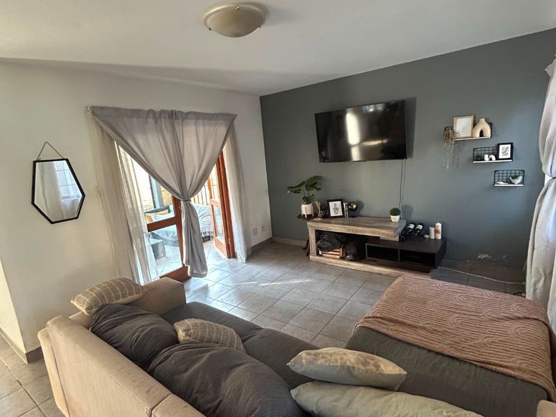 A living room featuring tiled flooring and a glass sliding door providing access to the outdoor area, with a feature wall.