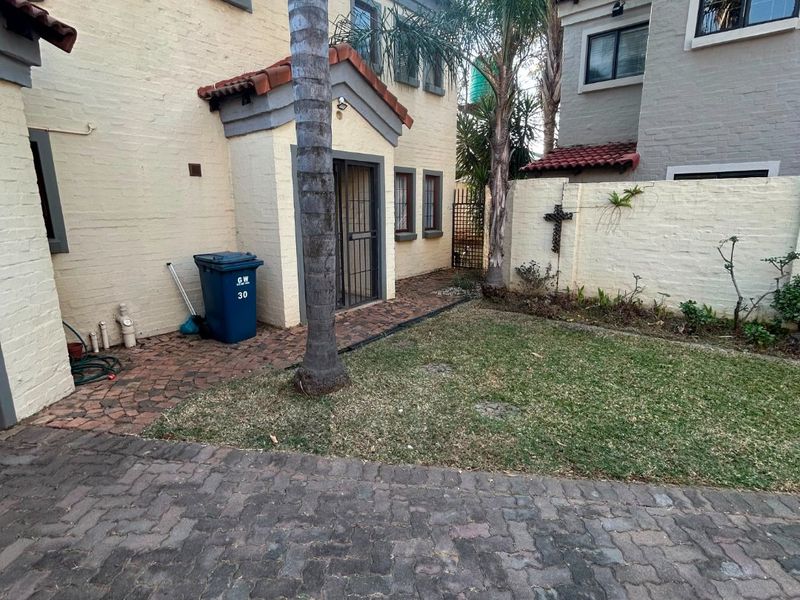 Front exterior view of a townhouse featuring a brick paved driveway, small garden area, and secure entrance with a security gate.