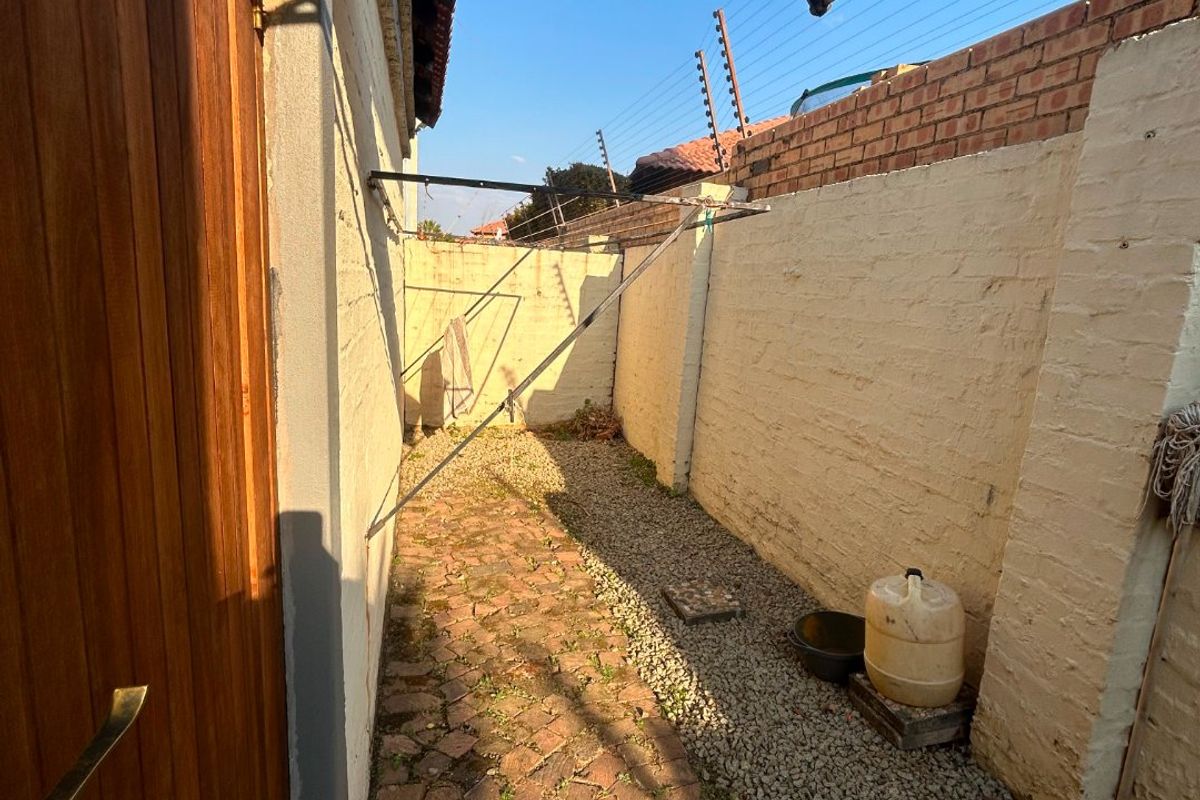 A narrow rear exterior courtyard featuring brick paving, gravel surfacing, a wall-mounted washing line, and perimeter walls with electric fencing.