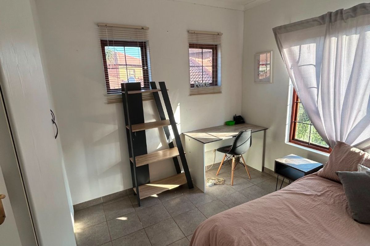 A functional bedroom featuring tiled flooring, built-in storage, and multiple windows providing natural light.
