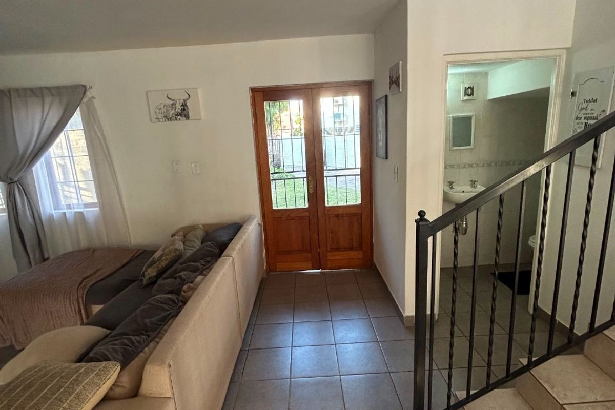 Living area featuring tiled flooring, a wooden double entrance door, and a staircase with wrought iron railing leading to an upper level.