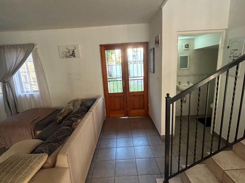 Living area featuring tiled flooring, a wooden double entrance door, and a staircase with wrought iron railing leading to an upper level.