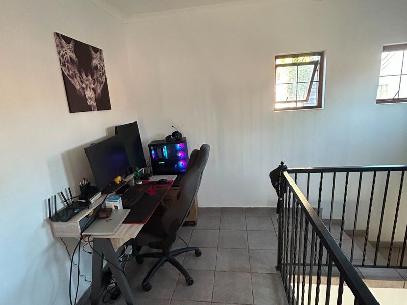 A functional landing area currently utilized as a home office, featuring tiled flooring and a wrought iron balustrade overlooking the lower level.
