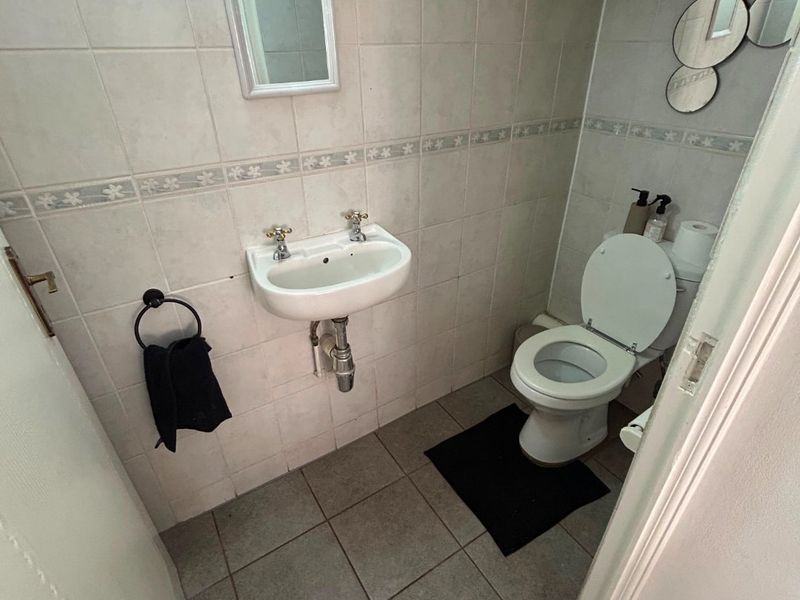 A functional guest bathroom featuring a wall-mounted basin, toilet, and neutral ceramic tiling throughout.