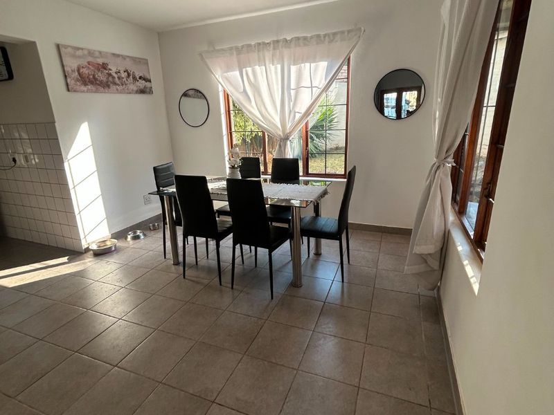 A bright dining room featuring neutral tiled flooring and large wooden-framed windows that provide natural light.
