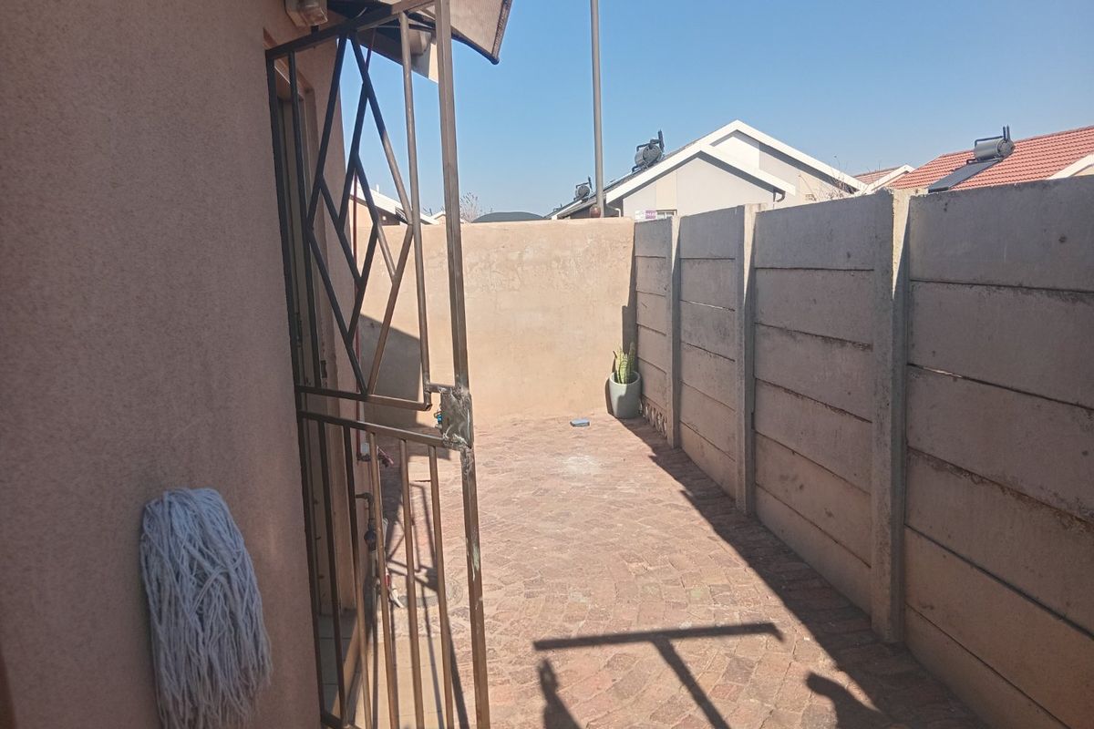 A private rear courtyard featuring paved flooring, enclosed by precast concrete boundary walls and secured with a metal gate.