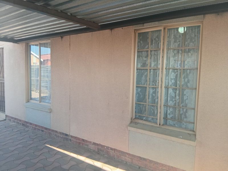 A covered patio area featuring paved flooring, plastered walls, and windows with security burglar bars.