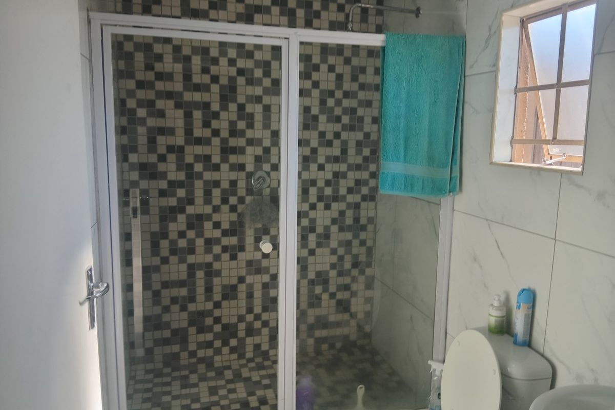 A functional bathroom featuring a shower enclosure with mosaic tiling, a pedestal basin, and a toilet, finished with marble-look wall tiles.