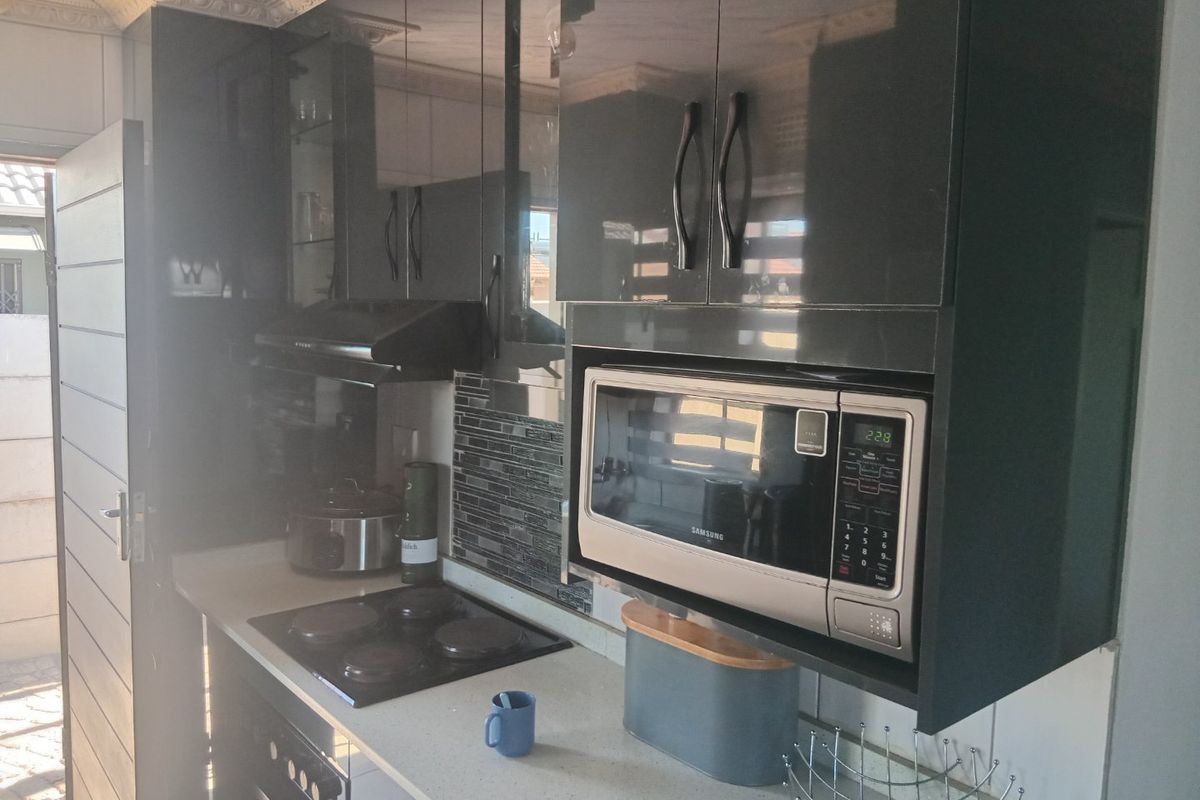 Modern kitchen featuring high-gloss cabinetry, stone countertops, a built-in microwave, and an electric hob with a tiled backsplash.