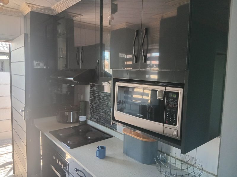 Modern kitchen featuring high-gloss cabinetry, stone countertops, a built-in microwave, and an electric hob with a tiled backsplash.