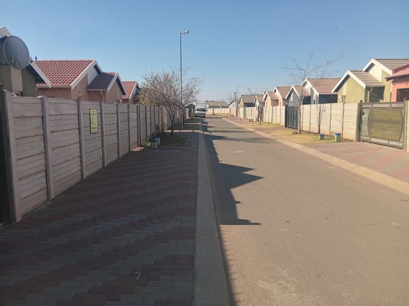 A street view of a residential neighborhood featuring paved sidewalks, asphalt roads, and uniform precast concrete boundary walls.