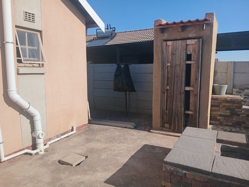 Rear exterior area featuring a concrete patio, built-in brick braai, and a small outdoor structure with a wooden door against a precast boundary wall.
