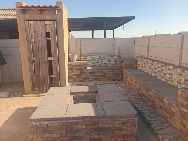 Outdoor patio area featuring a built-in brick fire pit and integrated bench seating, enclosed by a precast concrete boundary wall.