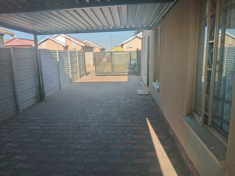 A covered carport area featuring paved flooring, enclosed by precast concrete walls and a secure metal gate.