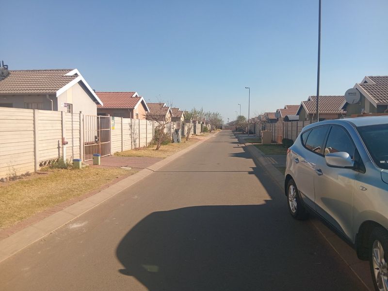 A view of a residential street featuring rows of houses with tiled roofs and precast concrete boundary walls.